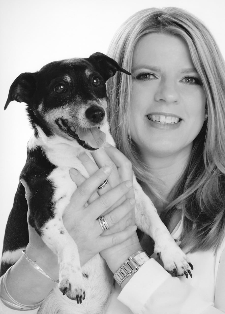 Black-and-white studio portrait of Alison Wagner, smiling, holding a Jack Russell terrier.