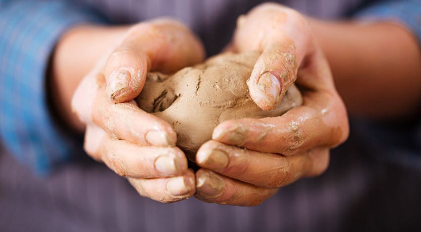 A pair of hands cupping a lump of wet clay.